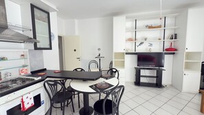 Un espace de vie compact comprenant une cuisine, un coin repas et un meuble pour les appareils multimédias.