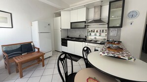 Une cuisine compacte avec des meubles blancs, un réfrigérateur Bosch, une cuisinière et un coin repas comprenant une table et des chaises.