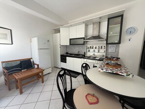 Eine kompakte Küche mit weißen Schränken, einem Bosch-Kühlschrank, einem Herd und einem Essbereich mit Tisch und Stühlen.