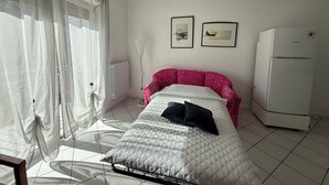 Une chambre à coucher avec un lit, un radiateur, un réfrigérateur et deux tableaux encadrés accrochés au mur.