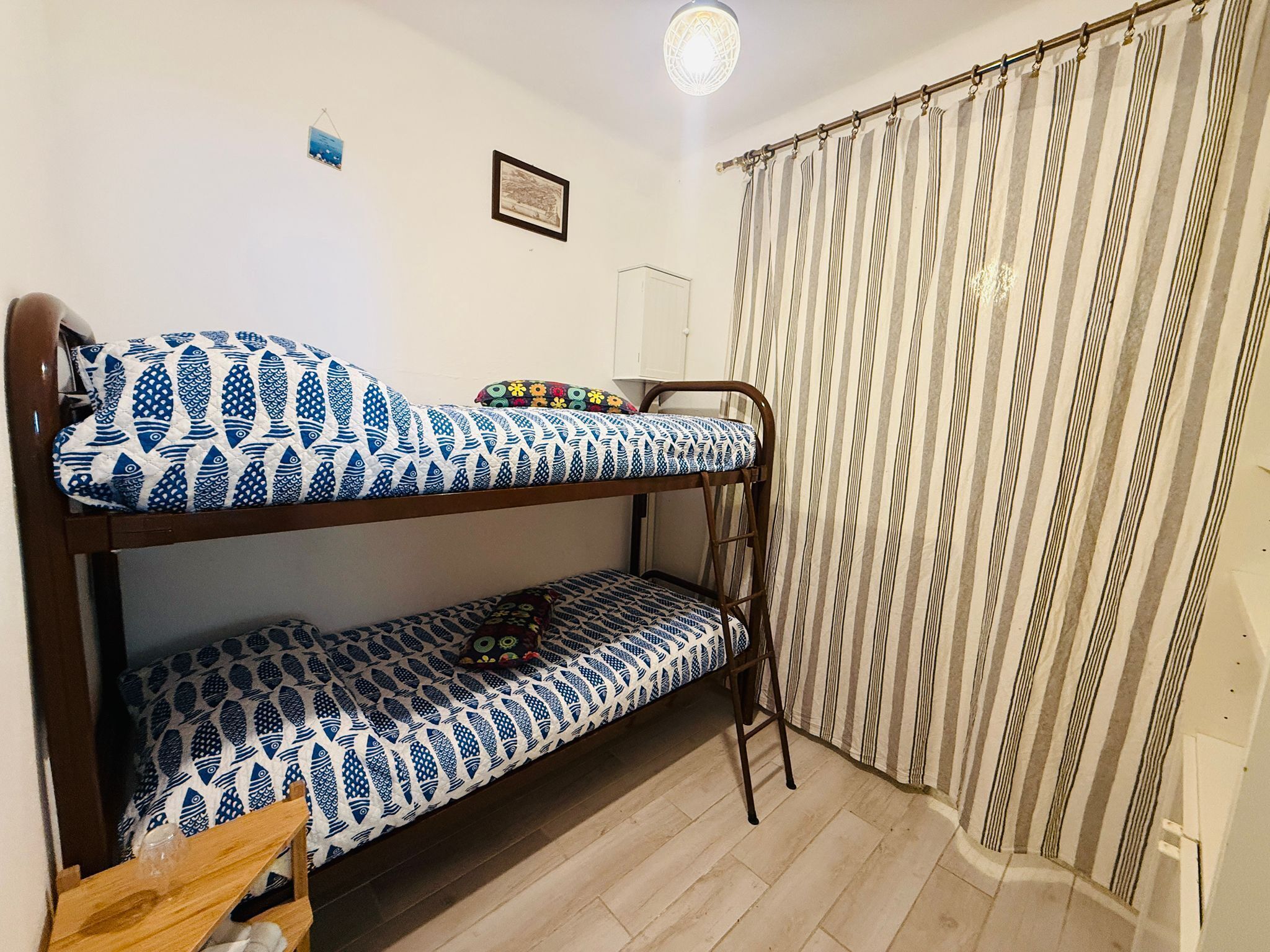 Une chambre avec un lit superposé, une structure en bois, des rideaux à rayures et un petit tableau encadré accroché au mur.