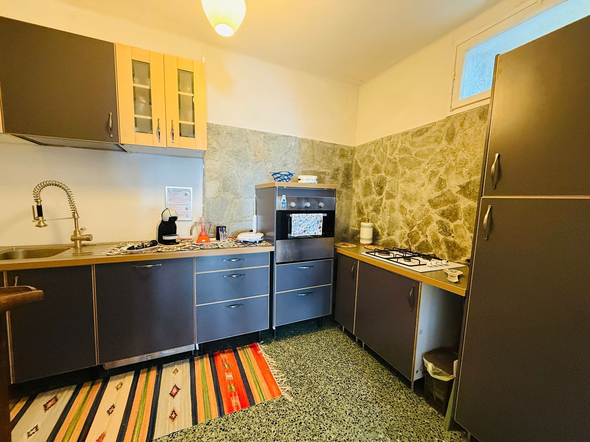 A compact kitchen with a gas stove, oven, and a sink. There are cabinets and a countertop with various items.