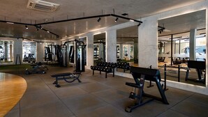 Ein großzügiger Fitnessraum mit unterschiedlichen Trainingsgeräten, großen Spiegeln und einem klaren, modernen Design.