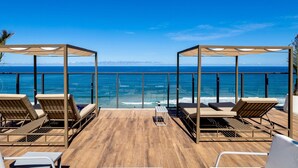 Eine Holzterrasse mit Liegestühlen und einer Pergola mit Blick auf den Ozean.