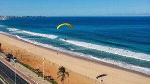 Ein Strand mit blauem Himmel, sandigem Ufer und einer Person, die Gleitschirm fliegt.