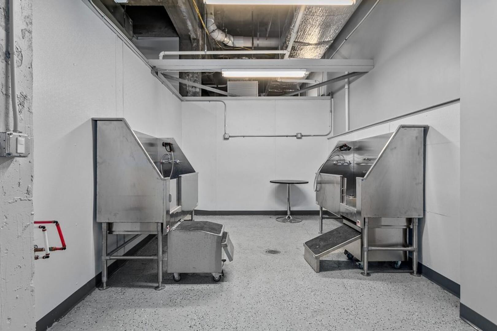 Eine saubere, industrial-stil Küche mit Edelstahlgeräten, einem kleinen runden Tisch und einem Rauchmelder an der Wand.