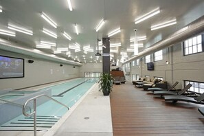 Une piscine intérieure dotée d’une terrasse en bois, de chaises longues et d’un escalier menant aux niveaux supérieurs.