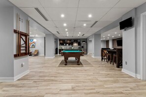 Une pièce spacieuse avec une table de billard, un coin bar et une cuisine à l’arrière-plan.