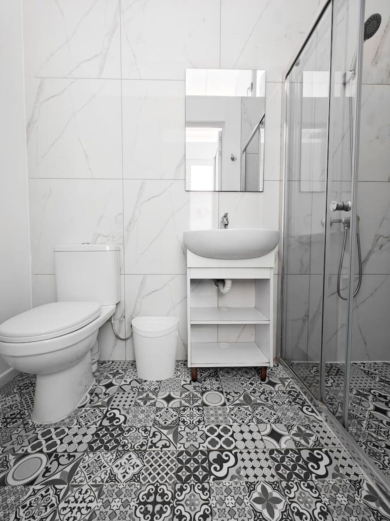 A bathroom with a toilet, sink, and shower. The floor has a patterned tile design.