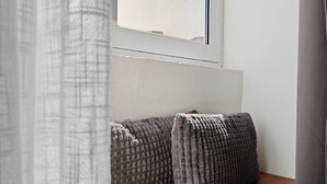 A window with a view of a wooden ledge and two grey cushions.