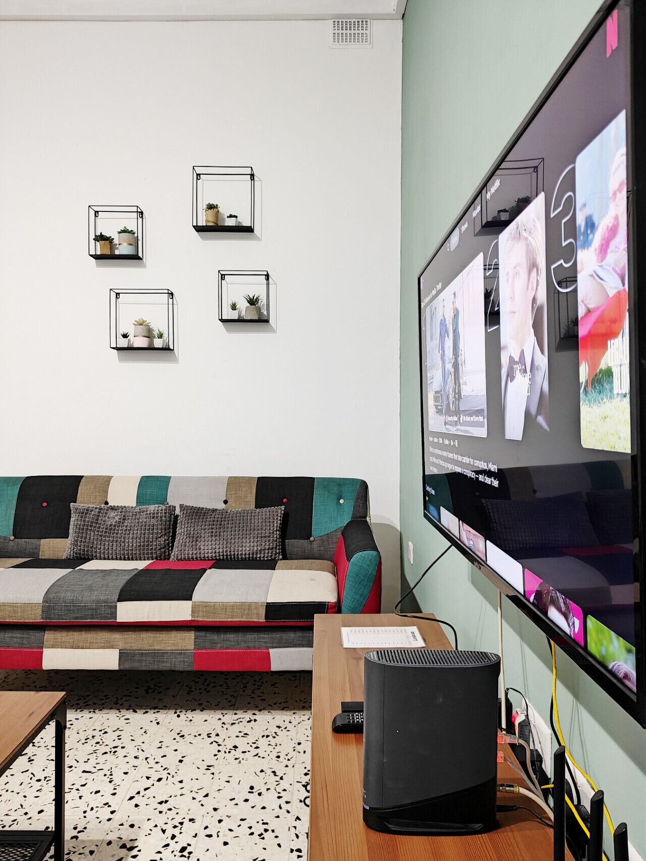 Una sala de estar moderna con un televisor de pantalla plana grande montado en la pared, un sofá de varios colores y una mesita con un control remoto.