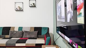 Una sala de estar moderna con un televisor de pantalla plana grande montado en la pared, un sofá de varios colores y una mesita con un control remoto.