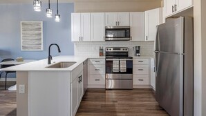 A modern kitchen with white cabinetry, stainless steel appliances, and a central island with a sink. - Landing | Amazing 1BD, Clubhouse (Goodyear)