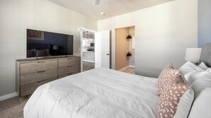 Habitació moderna amb un llit gran, televisió, armari i bany visible a través d'una porta oberta.