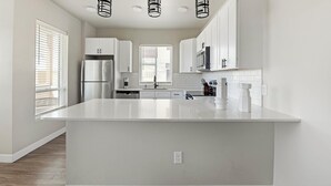Une cuisine moderne avec des meubles blancs, un grand îlot central et des luminaires suspendus.