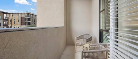 Un balcon avec deux fauteuils en osier, une fenêtre avec des stores et une vue sur les immeubles voisins.