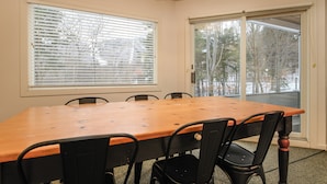 A dining room with a wooden table and black chairs, large windows with blinds, and a view of trees outside. - Sugarbush Escape  Fireplace and Shuttle Access (Warren)