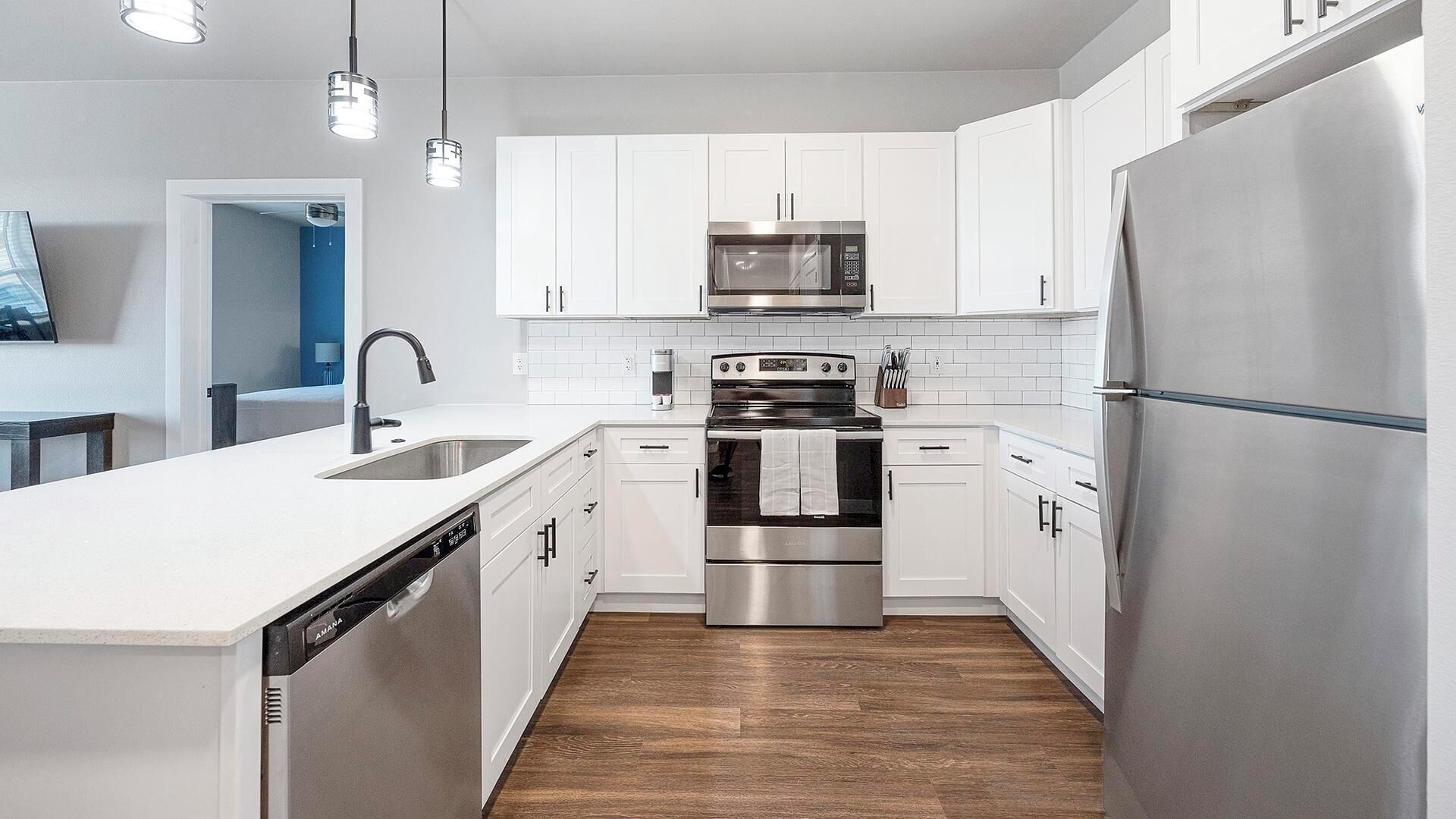 A modern kitchen with white cabinets, stainless steel appliances, a dishwasher, and a wooden floor.