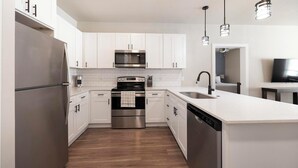A modern kitchen with stainless steel appliances, white cabinetry, and a wooden floor.