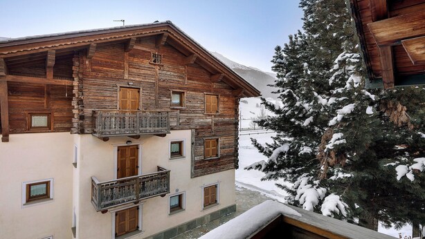 Un edificio de madera con balcones, un árbol cubierto de nieve y una montaña al fondo.