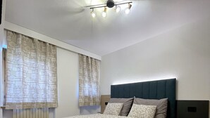 Un dormitorio con cama, cabecera, radiador y lámpara en el techo.