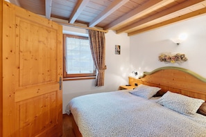 Une chambre avec une porte en bois, un lit avec une literie à motifs, une table de chevet et un luminaire fixé au mur.