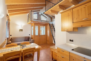 Un intérieur en bois comprenant une table à manger, des chaises, un canapé, un coin cuisine et un escalier menant à un niveau supérieur.