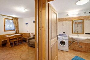 Una habitación compacta con una mesa de madera, sillas, lavadora y lavamanos.