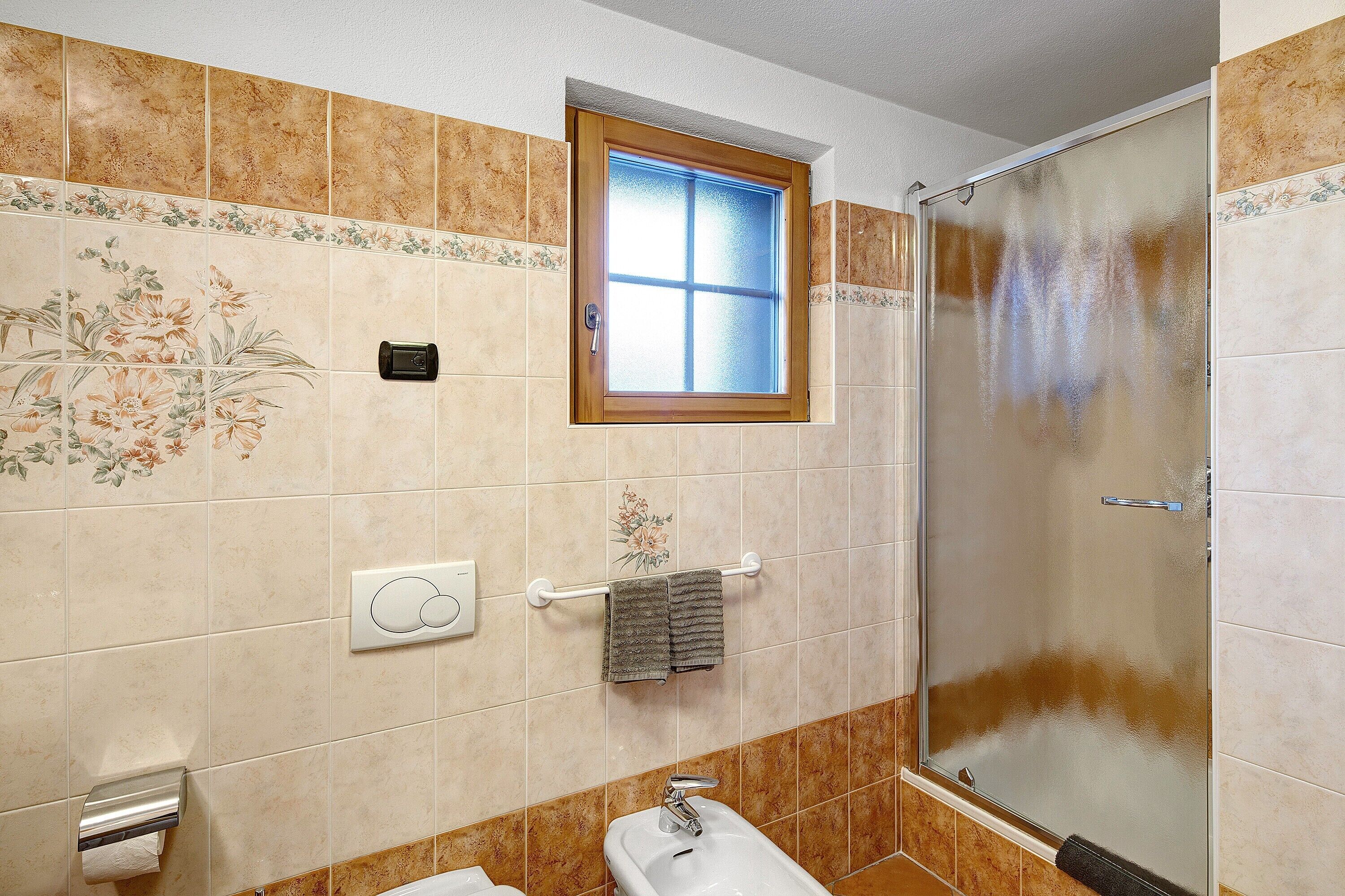 Un baño con ducha, inodoro, bidé, toallero y ventana.