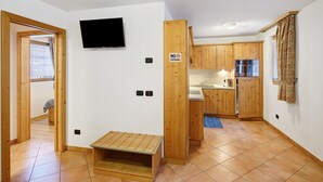 A compact kitchen with wooden cabinets, a built-in oven, and a television mounted on the wall. - Apartment 'Coccinella 2' with Mountain View (Livigno)