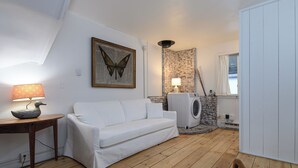 A cozy room with a white sofa, a lamp, a butterfly painting, a stone wall, and a washing machine. - Village Edge – Steps to the slopes at Sugarbush! (Warren)
