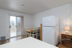 A small kitchen with a white refrigerator, a wooden table with four chairs, and a sliding glass door leading to a balcony. - Village Edge – Steps to the slopes at Sugarbush! (Warren)