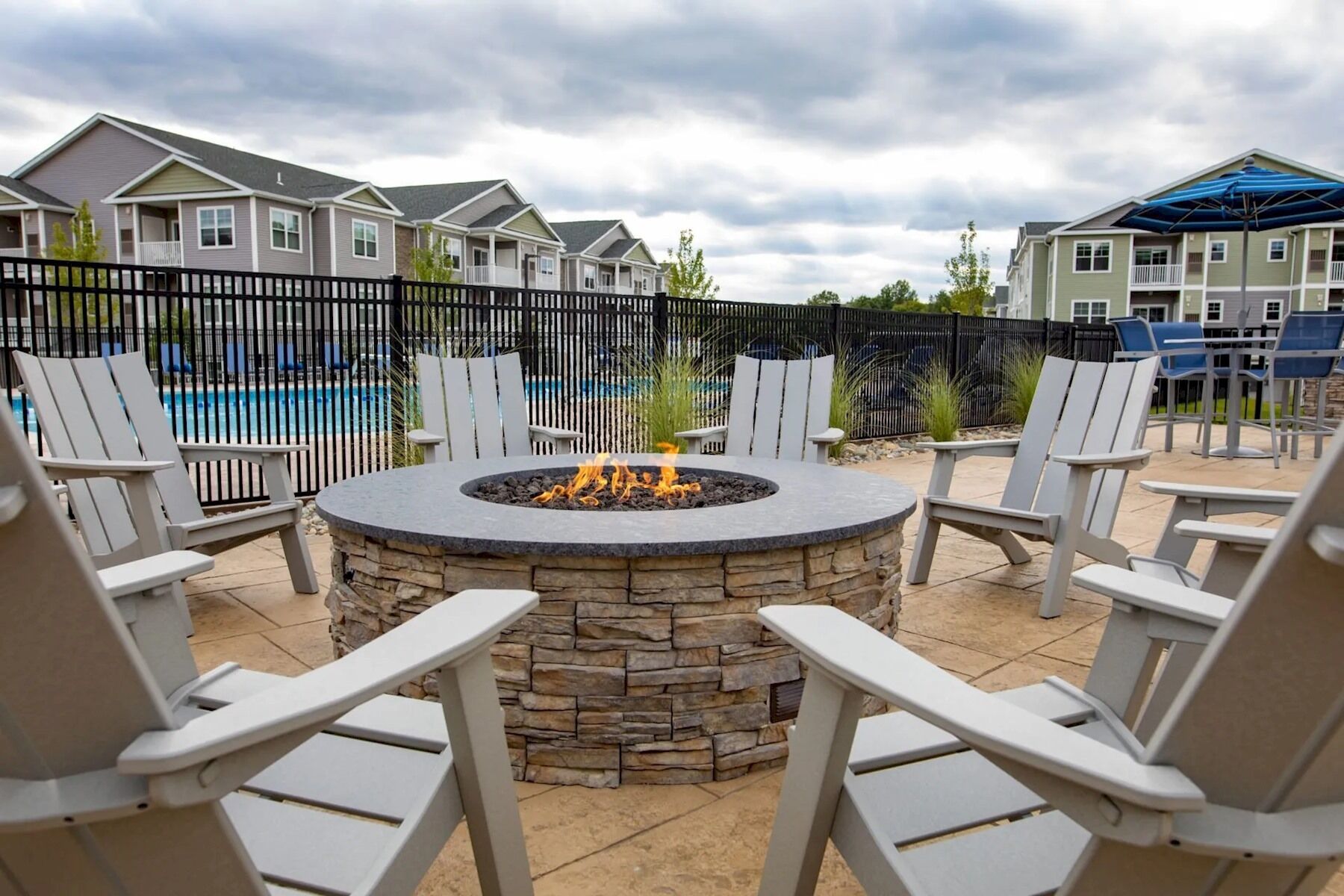 A circular stone fire pit surrounded by white Adirondack chairs in an outdoor patio area.