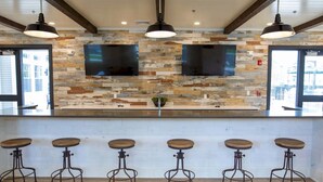 A bar area with a rustic stone wall, two flat-screen TVs, and five bar stools. - Landing Apartments Vernon (Vernon)