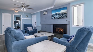 A living room with a fireplace, blue sofas, a coffee table, and a ceiling fan. - Charming 2BR/2BA Bridge-Level Condo at The Bridges Resort (Warren)