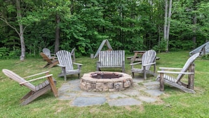 A stone fire pit surrounded by wooden Adirondack chairs in a grassy outdoor area with trees in the background. - Charming 2BR/2BA Bridge-Level Condo at The Bridges Resort (Warren)