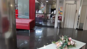 A lobby with a red seating area, a reception desk, and a white table with a floral arrangement. - HOTEL MEDICIS (Barcelona)