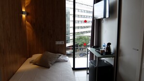 A bedroom with a bed, a desk with a computer, a TV, and a view of the outside. - HOTEL MEDICIS (Barcelona)