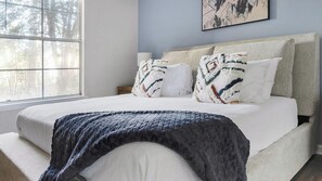 Un dormitorio con una cama grande, dos mesitas de noche, un ventanal y un cuadro en la pared.