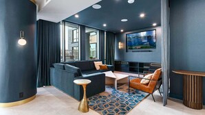 Un salon moderne avec un mur d’accent bleu foncé, un grand téléviseur à écran plat, un canapé, une table basse et un tapis à motifs.