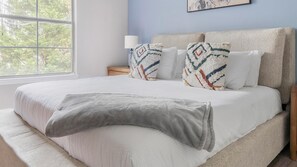 Une chambre à coucher avec un grand lit, une table de chevet, une lampe et une fenêtre donnant sur des arbres.
