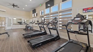 Un gimnasio con cintas de correr, bicicletas estáticas y un ventilador de techo.