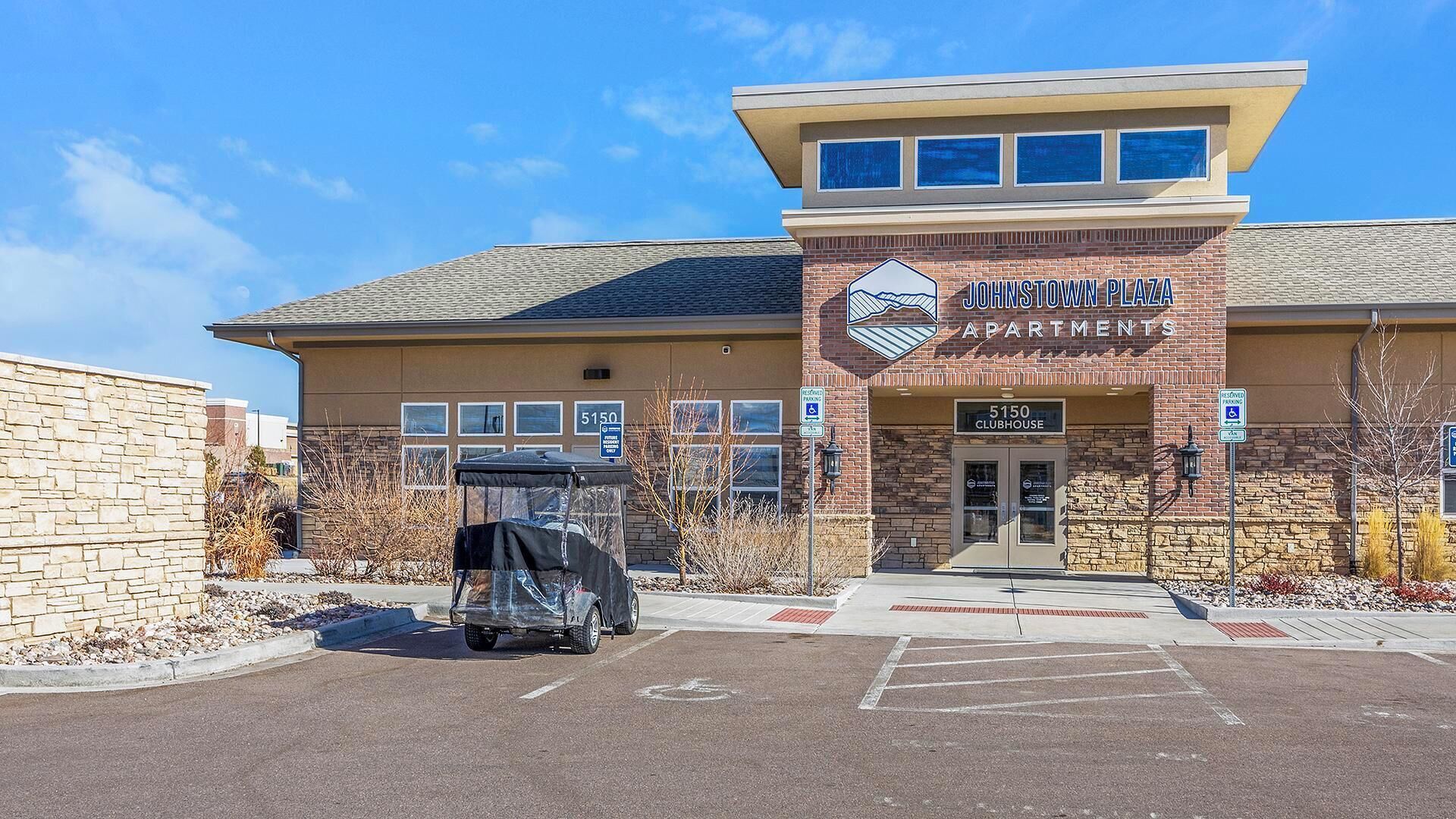 A Johnstown Plaza Apartments building with a brick facade, a clubhouse entrance, and a parking lot.
