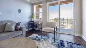 Una sala de estar moderna con un sofá gris, un sillón blanco, un escritorio con silla y un ventanal con vistas a una valla.