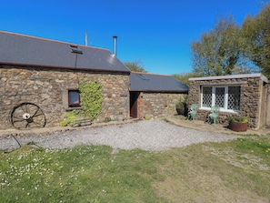A stone building with a gravel driveway, a wheelbarrow, and a small garden area. - Ramsgrove (Swansea)
