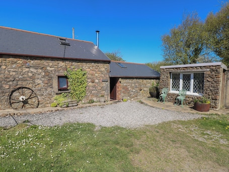A stone building with a gravel driveway, a wheelbarrow, and a small garden area.. Ramsgrove
