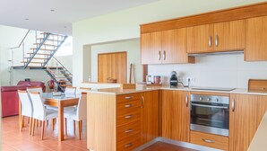 Een moderne keuken met houten kastjes, een inbouwoven en een eethoek met witte stoelen.