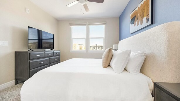 A bedroom with a large bed, a dresser, a television, and a ceiling fan. - Landing | Amazing 2BD, Clubhouse, Gym (Loveland)