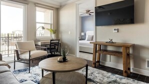 Un salon moderne avec une table ronde en bois, un canapé, un téléviseur fixé au mur et un balcon offrant une vue sur les immebles.