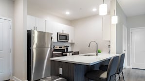 A modern kitchen with stainless steel appliances, a central island with bar stools, and pendant lighting. - Landing Apartments West Windsor (Windsor)
